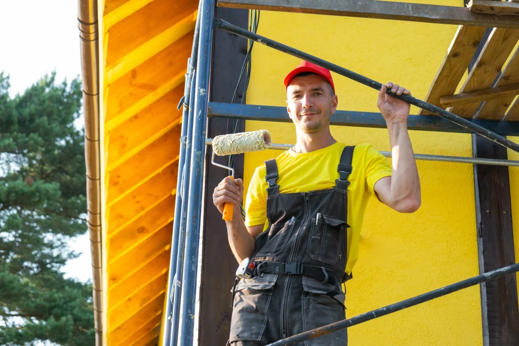 focused man painting exterior yellow wall on scaff 2026 09 25 02 20 06 utc